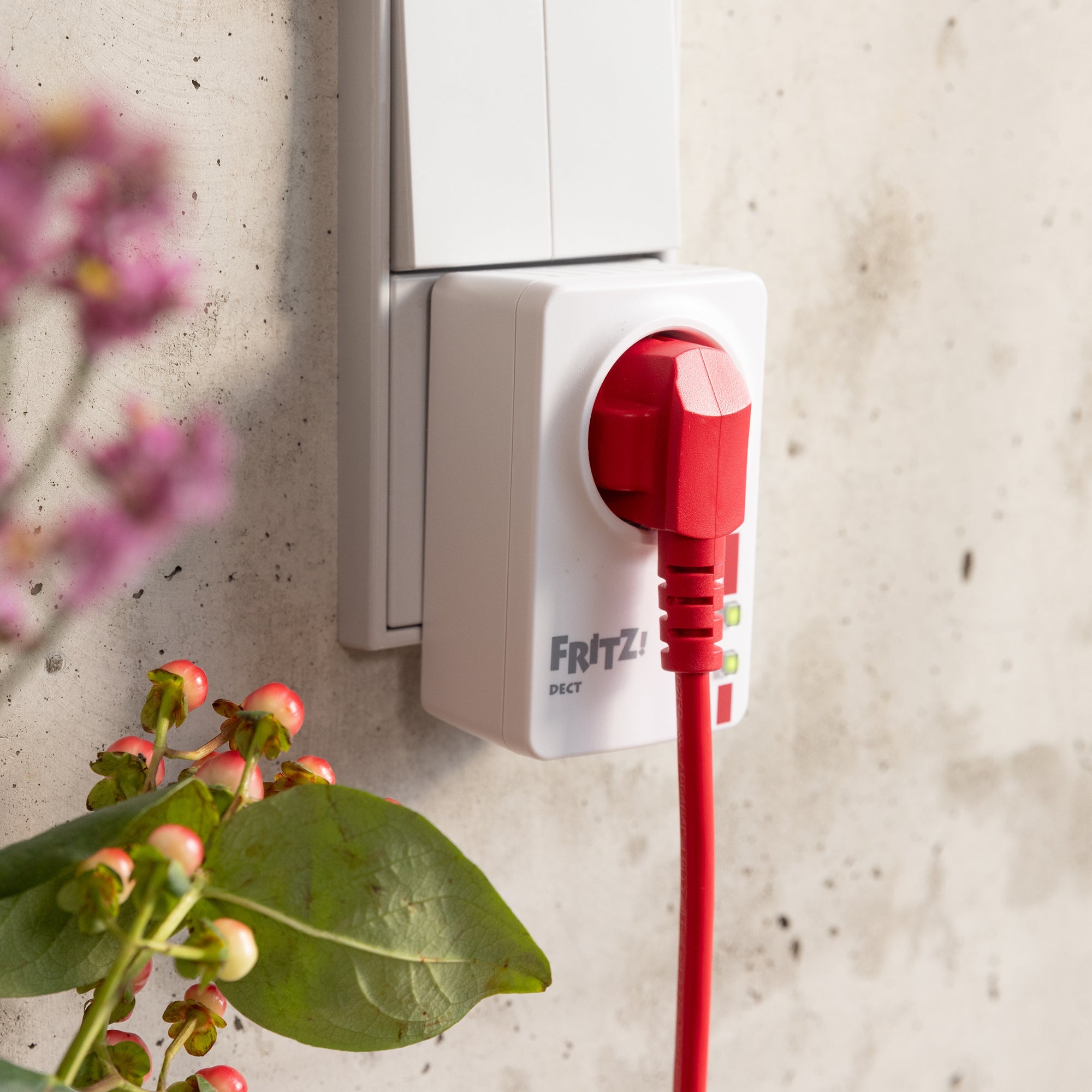 Intelligente Steckdose FRITZ!DECT 200 mit rotem Stecker, Pflanzen im Vordergrund, für Smart Home Automatisierung.